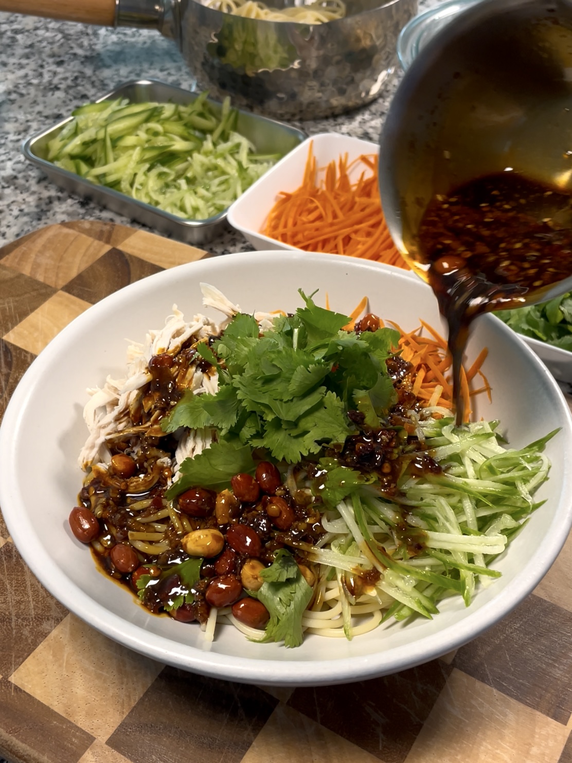 A bowl of Sichuan spicy noodles w/ shredded chicken, cucumber, and carrot, topped with cilantro