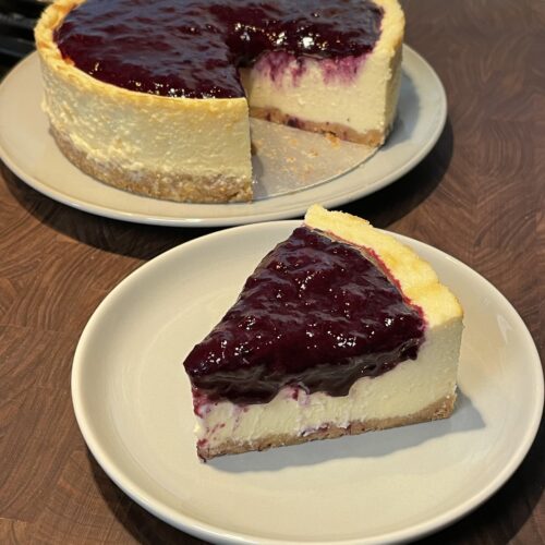 A slice of cheesecake with a graham cracker crust and blueberry compote on top