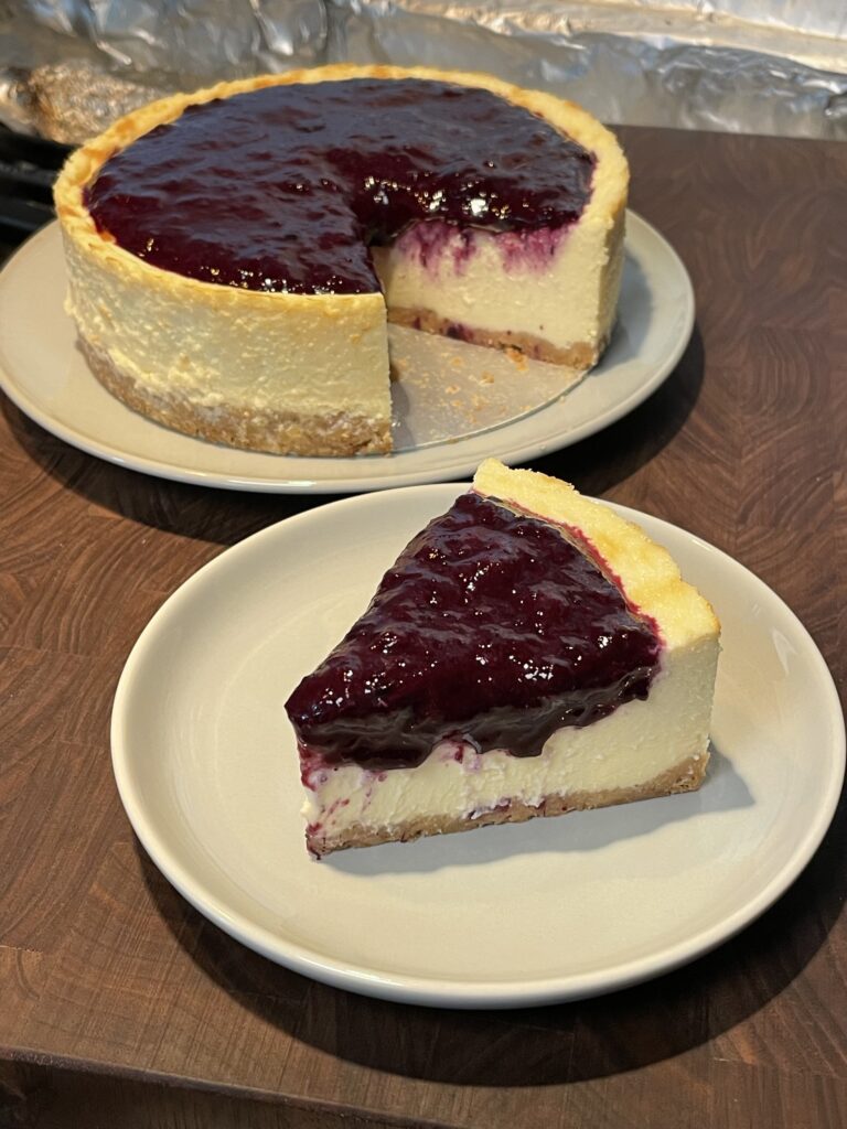A slice of cheesecake with a graham cracker crust and blueberry compote on top