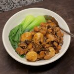 Bowl of rice topped with saucy diced chicken and quail eggs, with blanched bok choy on the side