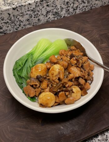 Bowl of rice topped with saucy diced chicken and quail eggs, with blanched bok choy on the side