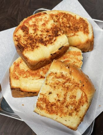 A stack of golden-brown, buttery homemade Texas toast, just like Raising Cane's, resting on a metal tray lined with parchment paper