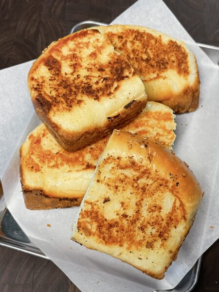 A stack of golden-brown, buttery homemade Texas toast, just like Raising Cane's, resting on a metal tray lined with parchment paper