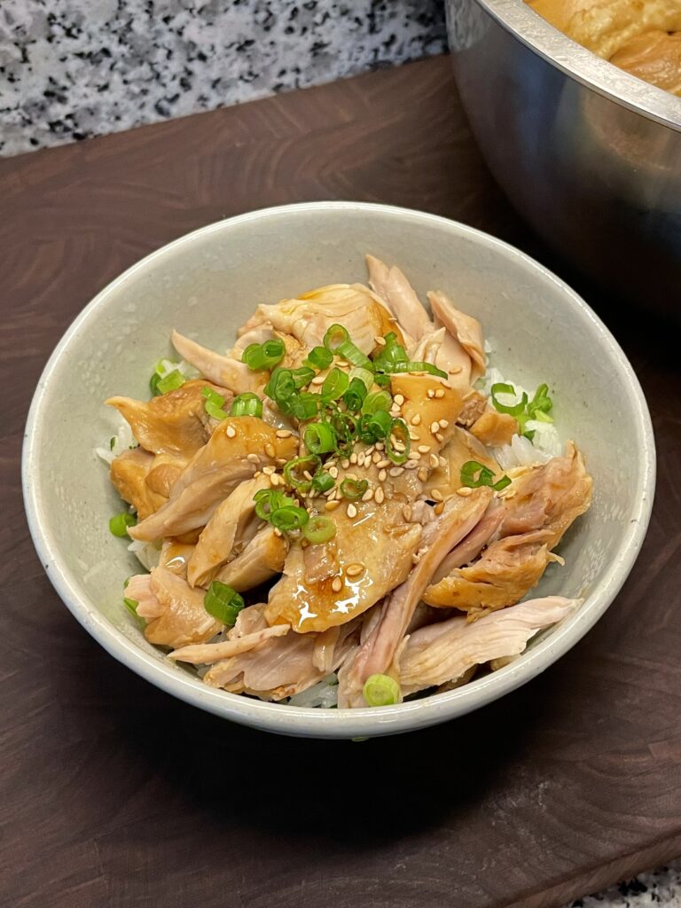 A bowl of shredded chicken on rice, drizzled with a thickened soy sauce and garnished with chopped scallions