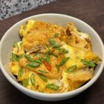 Bowl with a tofu and egg dish, garnished with sliced Thai red chili and scallions