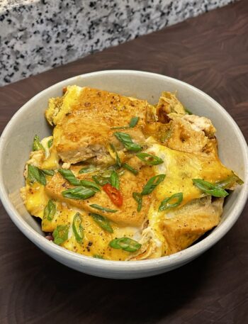 Bowl with a tofu and egg dish, garnished with sliced Thai red chili and scallions
