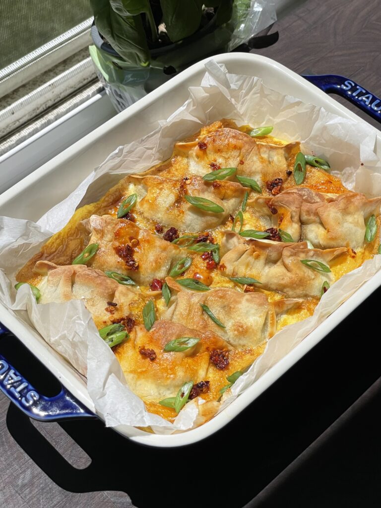 Dumplings in a baking sheet, surrounded by egg and topped with chili crisp and sliced green onions