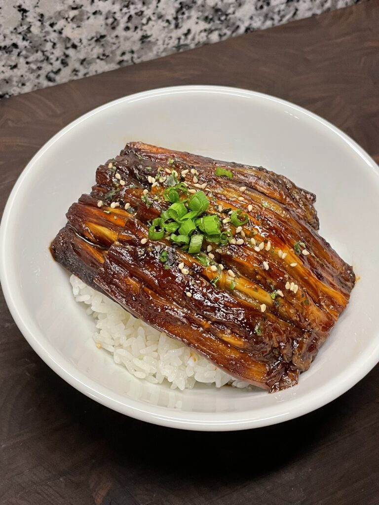 Soy glazed eggplant, garnished with furikake (Japanese seaweed and sesame seasoning) and chopped green onions, served over a bed of white rice