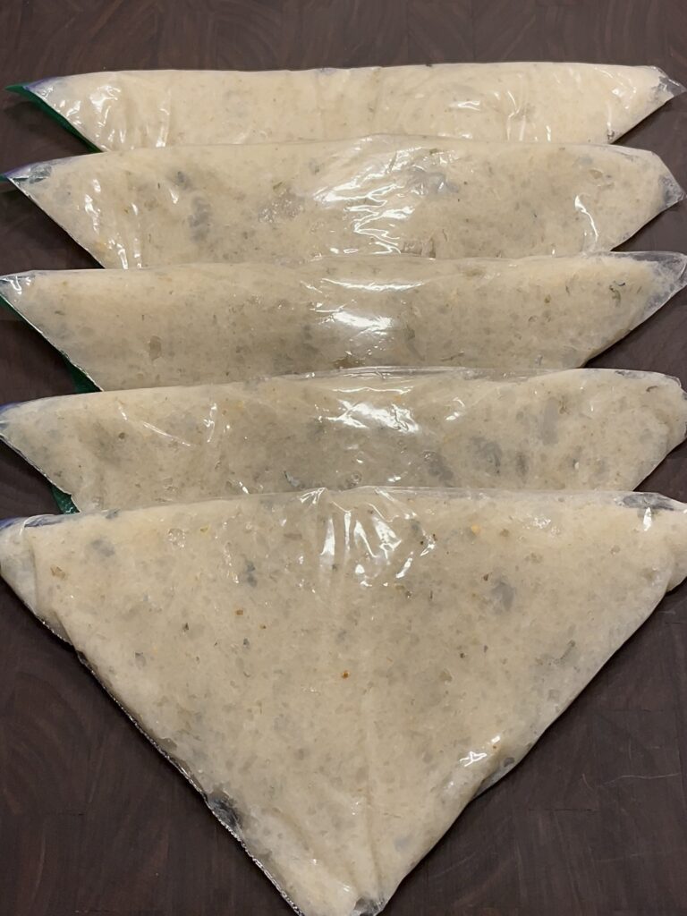 Five triangular plastic bags of white shrimp paste for Chinese hot pot, laid on a dark wooden cutting board