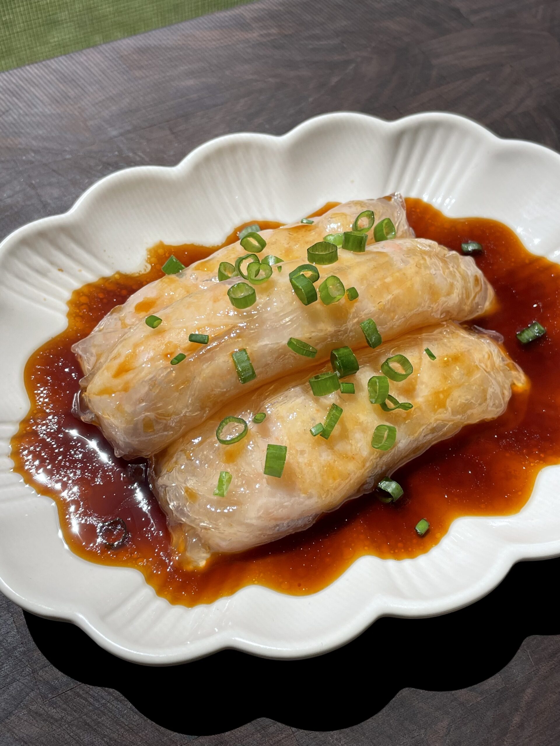 Cantonese shrimp rice rolls (cheung fun) on an ovular bowl, sitting on a brown sauce under the sun