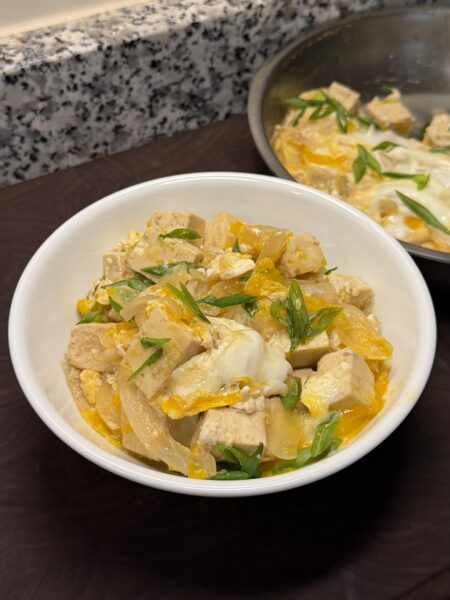 Wide white bowl topped with a tofu and egg dish over rice, garnished with sliced scallions